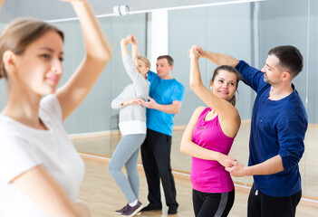 Fototapeta na wymiar Smiling dancing people practicing bachata movements in dance studio for adults