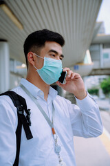 Businessman wear mask hold a phone at bus stop in city.