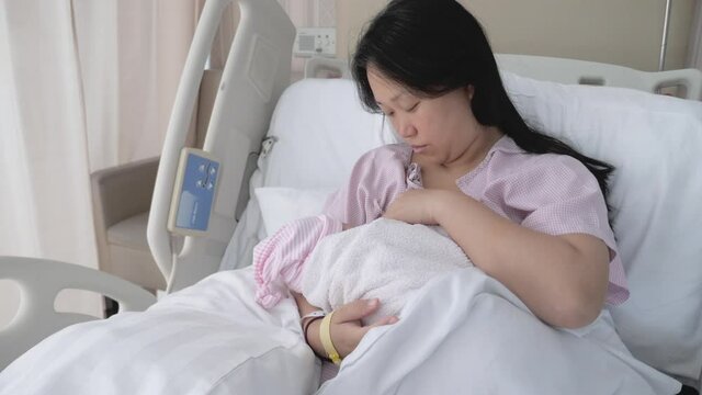 A tired Asian mother breast feeds her newborn child after birth and then quickly takes a rest. 