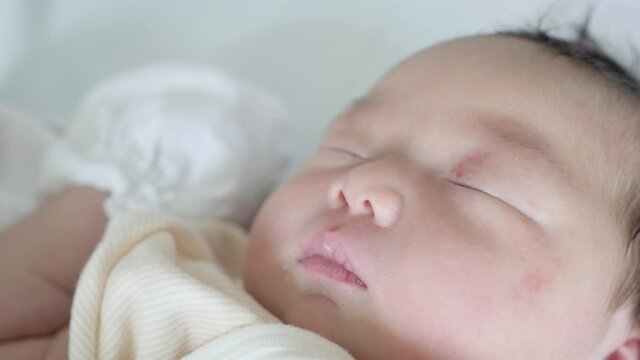 A newborn Asian baby girl asleep after delivery wearing gloves.