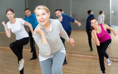Fototapeta na wymiar Portrait of emotional middle-aged woman doing exercises during group class in dance center