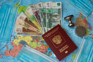 Russian foreign passport, fan of money and lot of medical masks on the background of colorful world map. Travel and border crossings during Coronavirus pandemic