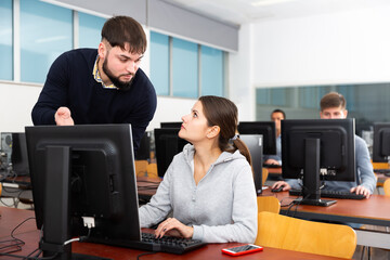 Adult teacher helping student in computer class in university