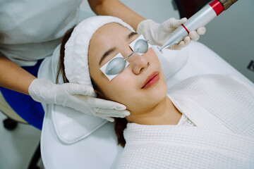 Asian woman getting laser and ultrasound face treatment in beauty clinic.