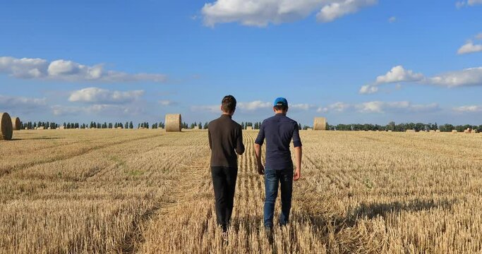 A young farmer with a digitalization specialist in a field with bales collects data on the wheat harvest by entering them into a tablet