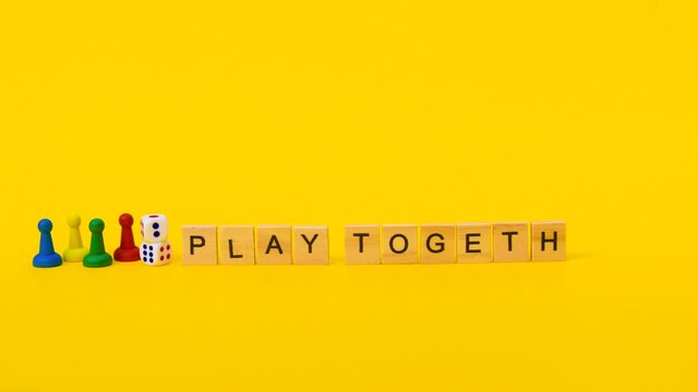Inscription "play together" on wooden blocks gradually appears on yellow background next to multi colored chips for the game: blue, yellow, green and red near two dice