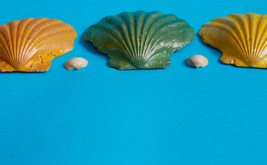 Marine layout. Three seashells painted orange, yellow, and green, and two small white seashells on a blue background.