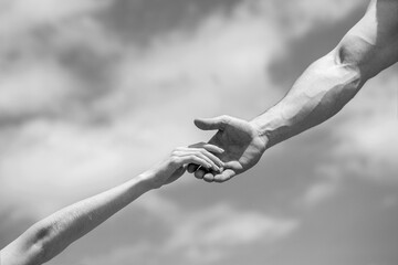 Hands of man and woman on blue sky background. Lending a helping hand. Solidarity, compassion, and charity, rescue. Black and white