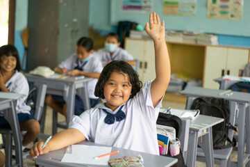 The little girl sitting in the classroom studying She raised her hand to answer the question.