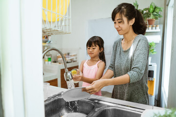 Helping hand. Cute little Girl Help Her Mother In Washing Dishes At Family Kitchen