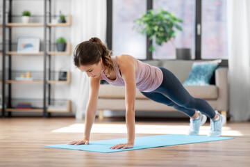 Naklejka na ściany i meble fitness, sport, training and people concept - young woman doing high plank exercise on mat at home