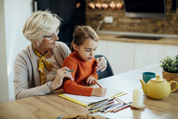 Little girl and her grandmother enjoying together while drawing on the paper.