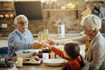 Happy grandparents and granddaughter toasting during Thanksgiving lunch at home.