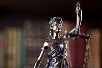 Law and justice concept. Themis sculpture in lawyers office. Bookshelf with legal books in background.