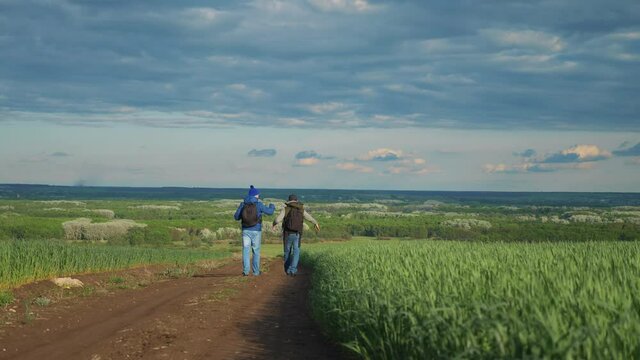 teamwork travel. two man hikers with backpacks walk along a trail next to a field with green grass in nature. concept adventure travel hiking healthy lifestyle. two tourists walk walking talking