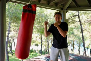 Joyful young man boxing a red pear against the background of a green forest on an outdoor in the...