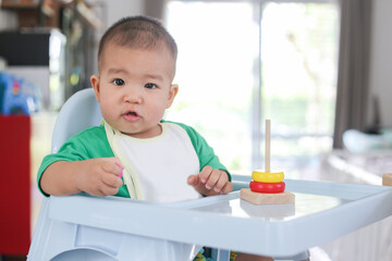 A baby of asia wearing bright green clothes is playing rainbow tower toys.