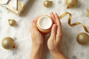 Female hands hold jar of cosmetic cream on background with Christmas accessories