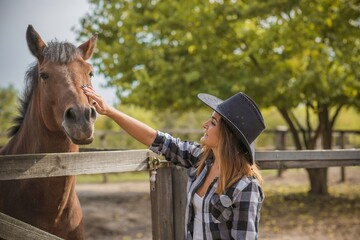 American woman on a horse farm. Portrait of girl in cowboy hat with a  horses. Hippotherapy at nature