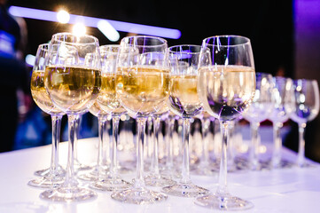 Glass of white wine on a table. Many glass wine in a row on bar counter. Glasses with wine. Filled with half and stand on the holiday table. Furshet.