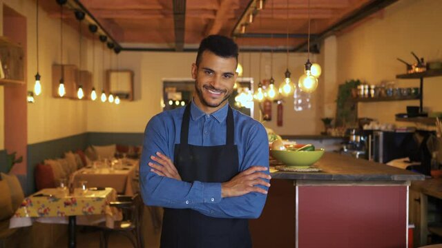 Cheerful positive handsome restaurant owner with crossed arms proud by himself looking at camera. Portrait of an african american attractive waiter or owner, at a restaurant. Small business concept.