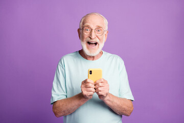 Photo portrait of excited screaming man holding phone in two hands isolated on vivid violet colored background
