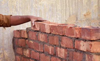 An Indian professional construction worker laying bricks during construction of a wall. Details of hand adjusting bricks