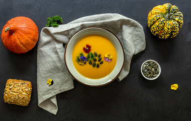 Autumn vegan pumpkin cream soup with edible flowers, seeds and bread