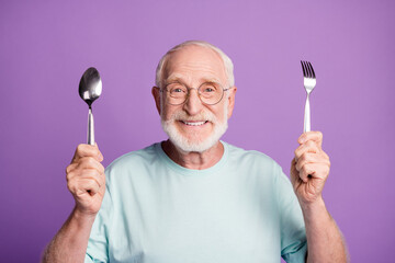 Photo of positive cheerful old man hold fork spoon ready eat wear good look t-shirt isolated over...