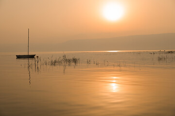 Sunrise over the lake. Boat floating on the calm water under amazing sunset.