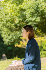 Naklejka premium 秋の公園でコーヒーを飲みながら読書している女性の姿