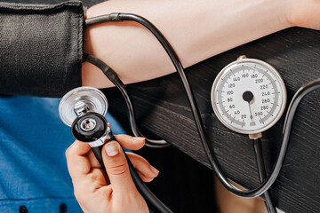 Doctor measures blood pressure with a tonometer to a woman patient at a medical appointment in a clinic