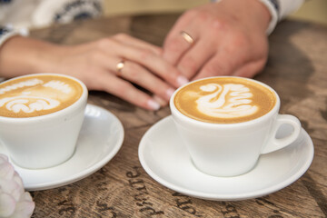 Wedding rings on the hands of brides. Fragrant, hot cappuccino on the table.
