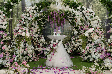 Wedding ceremony arch decorated with roses. In the middle is a table with candle composition.