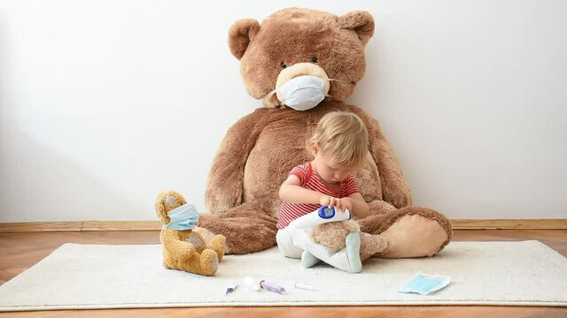 Cute little child playing with his sick teddy bears wearing medical mask against viruses. Role playing, child playing doctor with plush toy. Children and flu, coronavirus illness concept.
