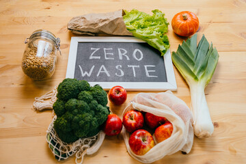 Zero waste lifestyle, flat lay, top view on wooden table background with broccoli, salad, apples, pumpkin, black board with text Zero Waste, eco friendly green vegetableshealthy food concept.
