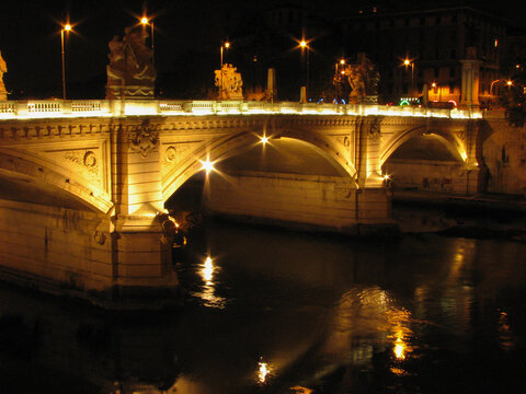 The Ponte Cavour Bridge in Rome, designed by the architect Angelo Vescovali, over the Tiber River and lit up by yellow lights at night.  Image has copy space.