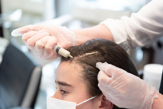 Working during Coronavirus pandemic concept. A hairdresser applying a treatment to a teenager client wearing a face mask.