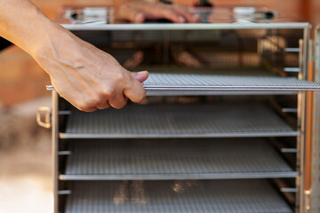 Human hands, taking out empty metal pan from dehydrating machine. Equipment for producing dry meat...
