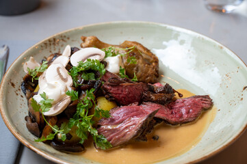 A meal based around butchers steak with mushrooms and tomatoes served in a gray rustic plate in restaurant setting