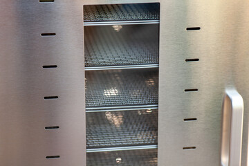 New dehydrating machine with closed door and many empty mesh pans inside. Equipment for producing...