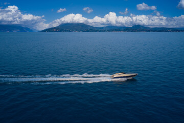 Large speedboat moving at high speed in the background of the coastline mountains and cumulus clouds. The boat is gray-blue combined color. Large speed boat moving at high speed side view.