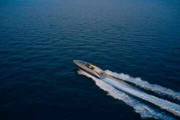 Large speed boat moving at high speed side view. The boat is gray-blue combined color. Top view of a boat sailing to the blue sea. Drone view of a boat  the blue clear waters at sunset.