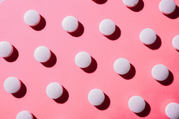 many white medical pills in a row on a pink background. pills cast a shadow. pill pattern