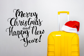 On a yellow plastic suitcase wearing a red Santa Claus hat on a light background. Added the inscription Merry Christmas and Happy New Year