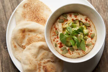 Hummus with avocado and herbs in white bowl