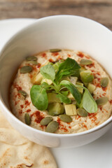 Hummus with avocado and herbs in white bowl