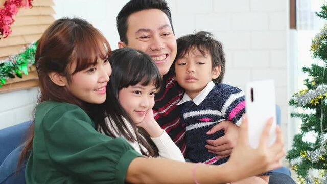 Selfie of happy asian family in quarantine merry christmas enjoy selfie or take photo shoot group shot sitting together at home apartment enjoy leisure time with X'mas tree..