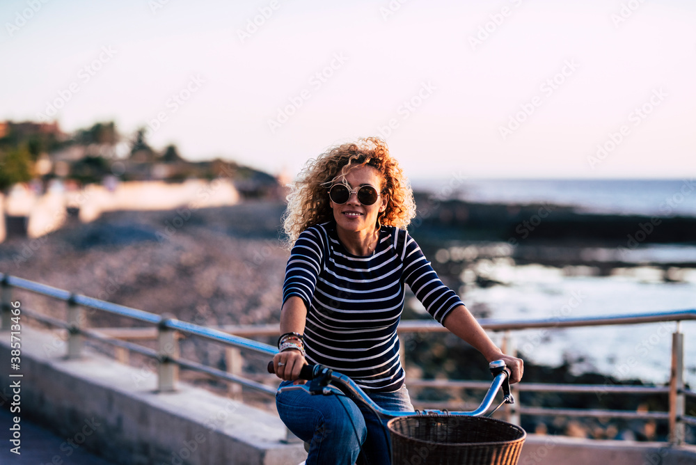 Wall mural Cheerful adult mature beautiful woman enjoy the ride and outdoor leisure activity alone in healthy lifestyle - ocean blue coast in background for happy people