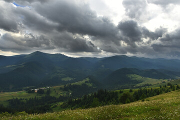 Mountain summer landscape. Green mountain slopes, glades with different colors and the sky with beautiful clouds.